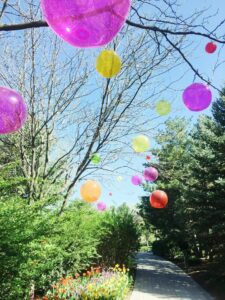 Vibrant balloons float above a garden path in a sunny park, creating a festive summer scene.